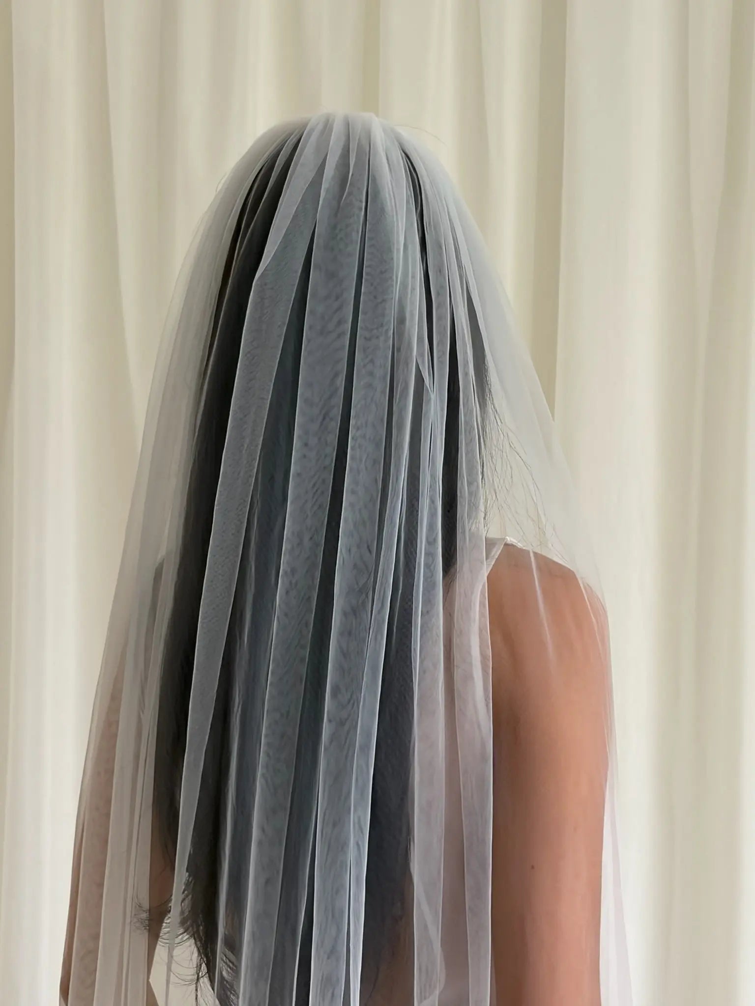 Person wearing a white wedding dress with a long plain veil against a plain background