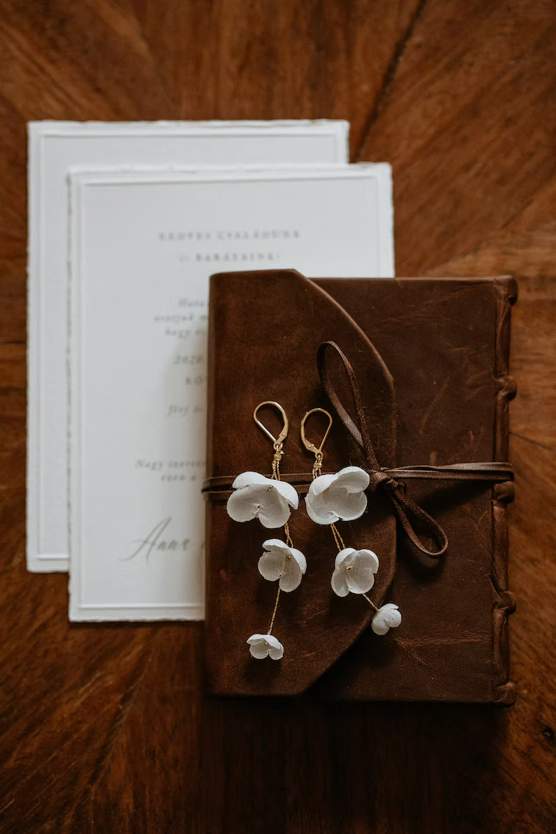 a flat lat of wedding invitations with a pair of silk flower bridal earrings