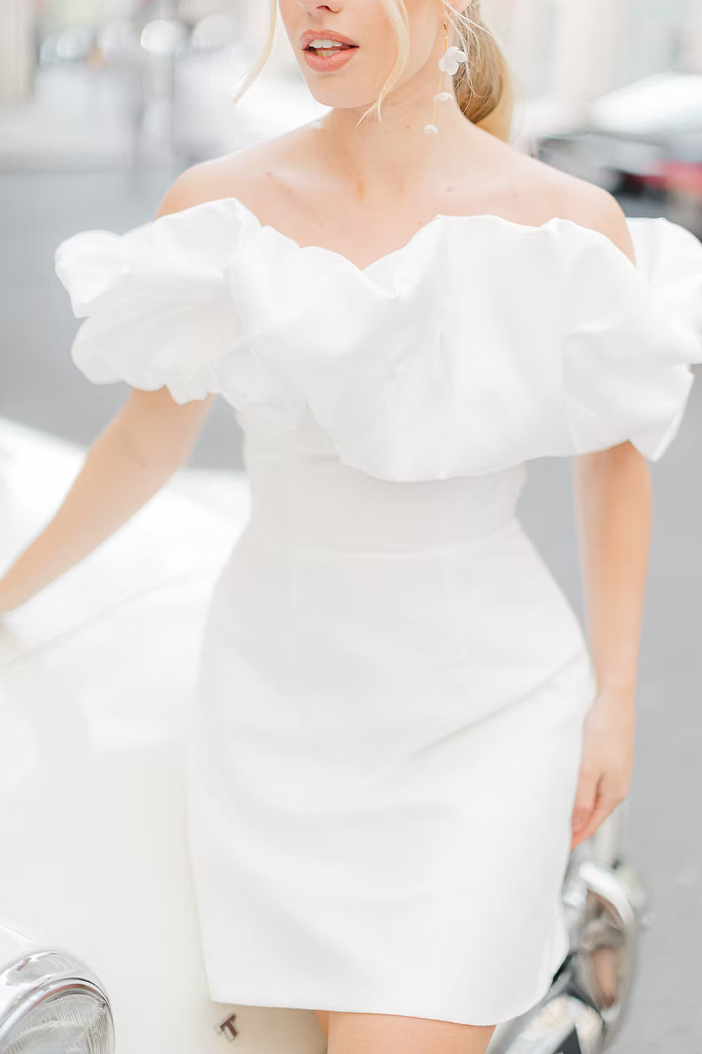 a woman wearing a white off-shoulder dress against a city background wearing silk flower bridal earrings