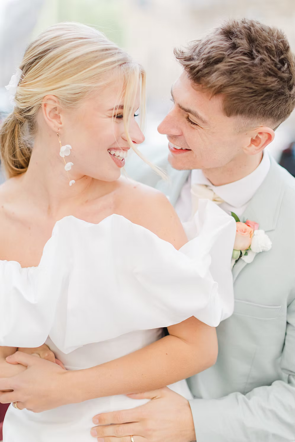 a married couple with the woman wearing a white off-shoulder dress against a city background wearing silk flower bridal earrings