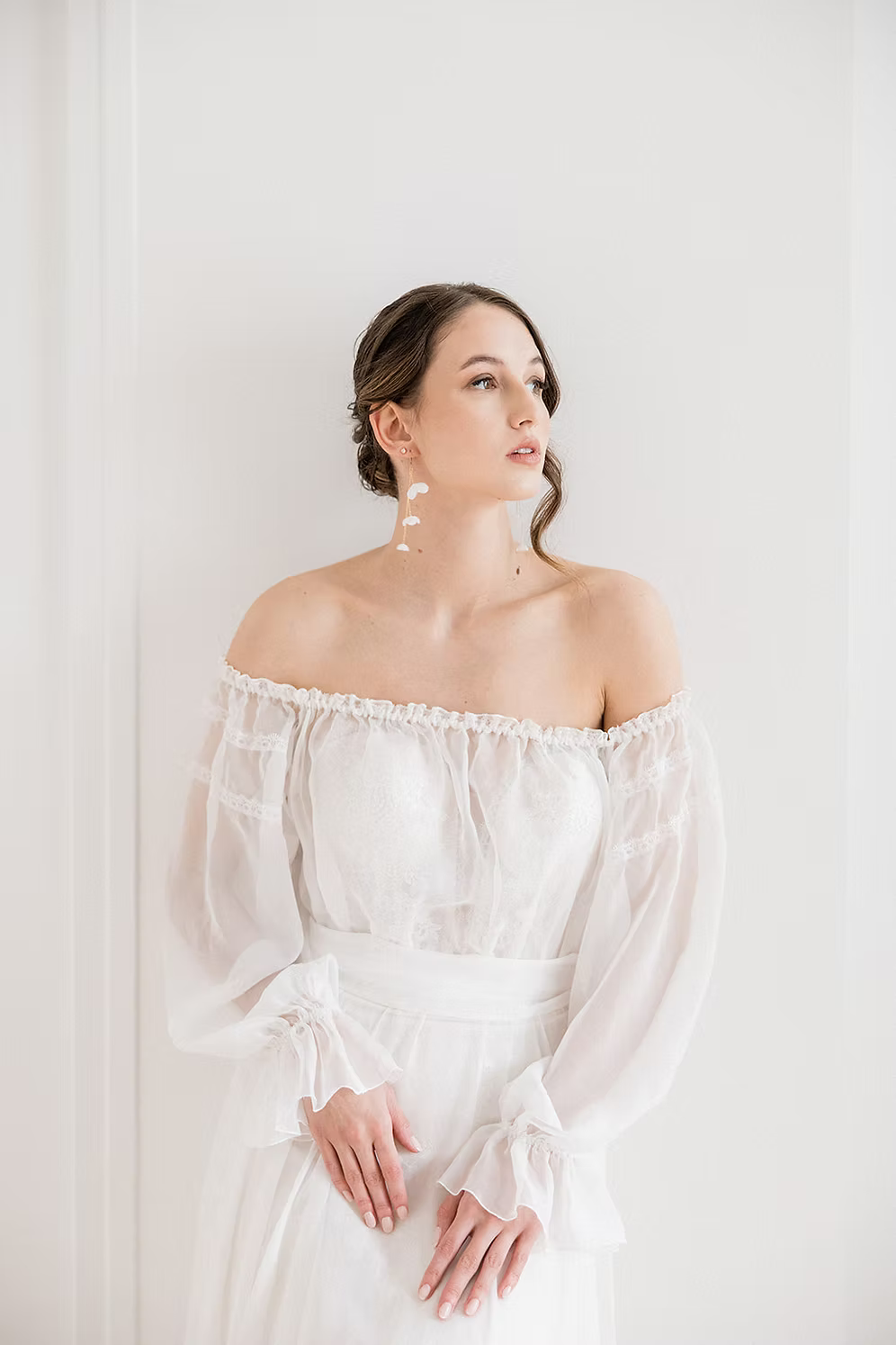 Woman wearing a white off-shoulder dress against a plain background wearing silk flower bridal earrings