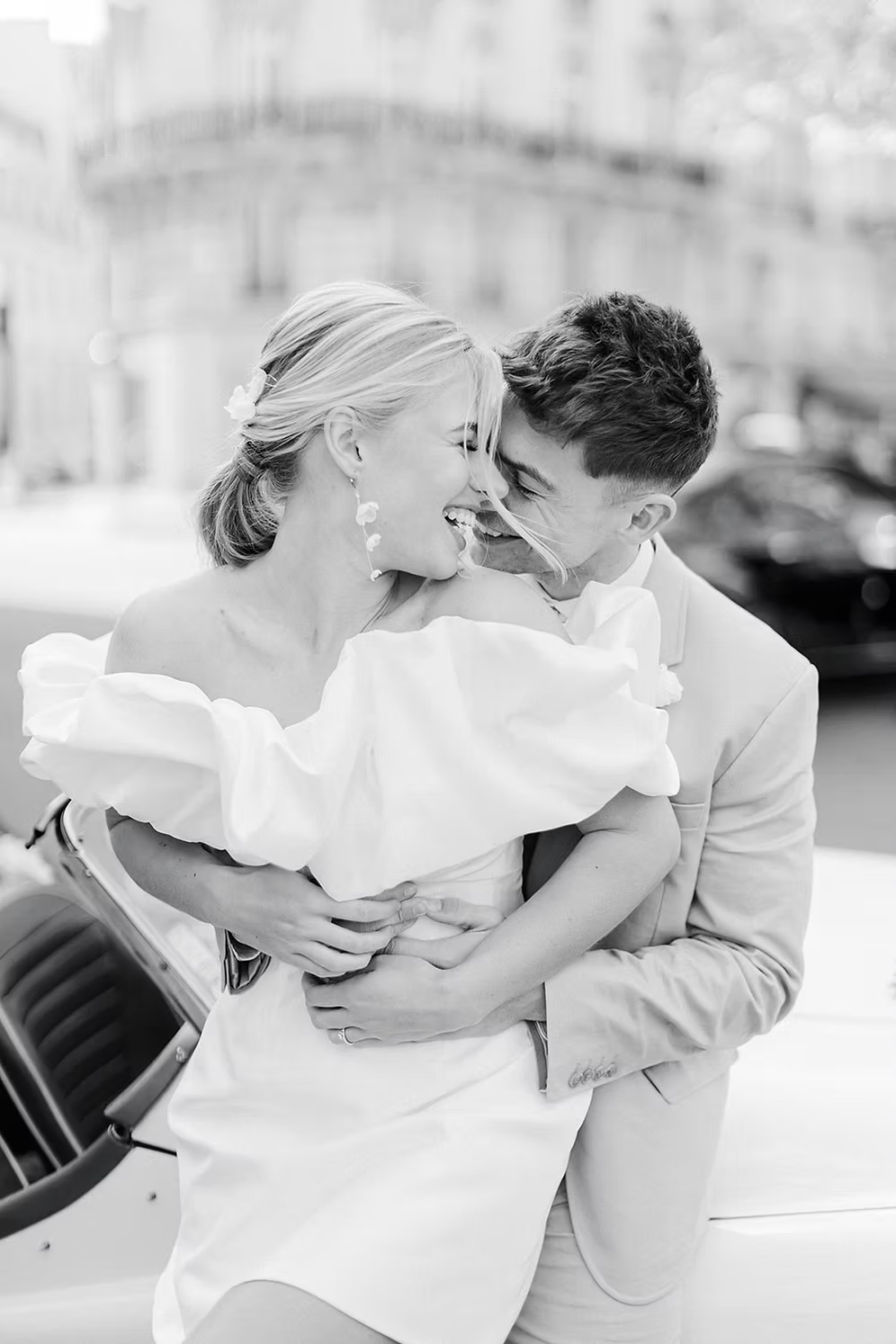 a married couple with the woman wearing a white off-shoulder dress against a city background wearing silk flower bridal earrings