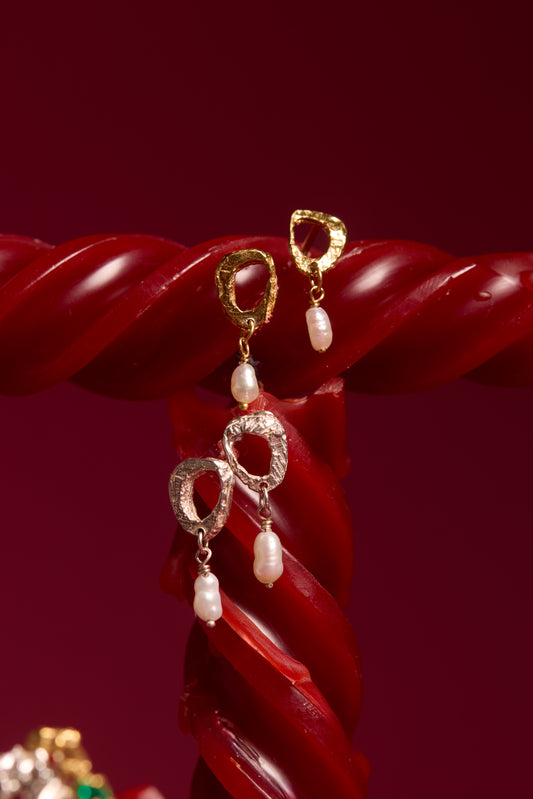 Gold and silver earrings with pearl drops on a red background