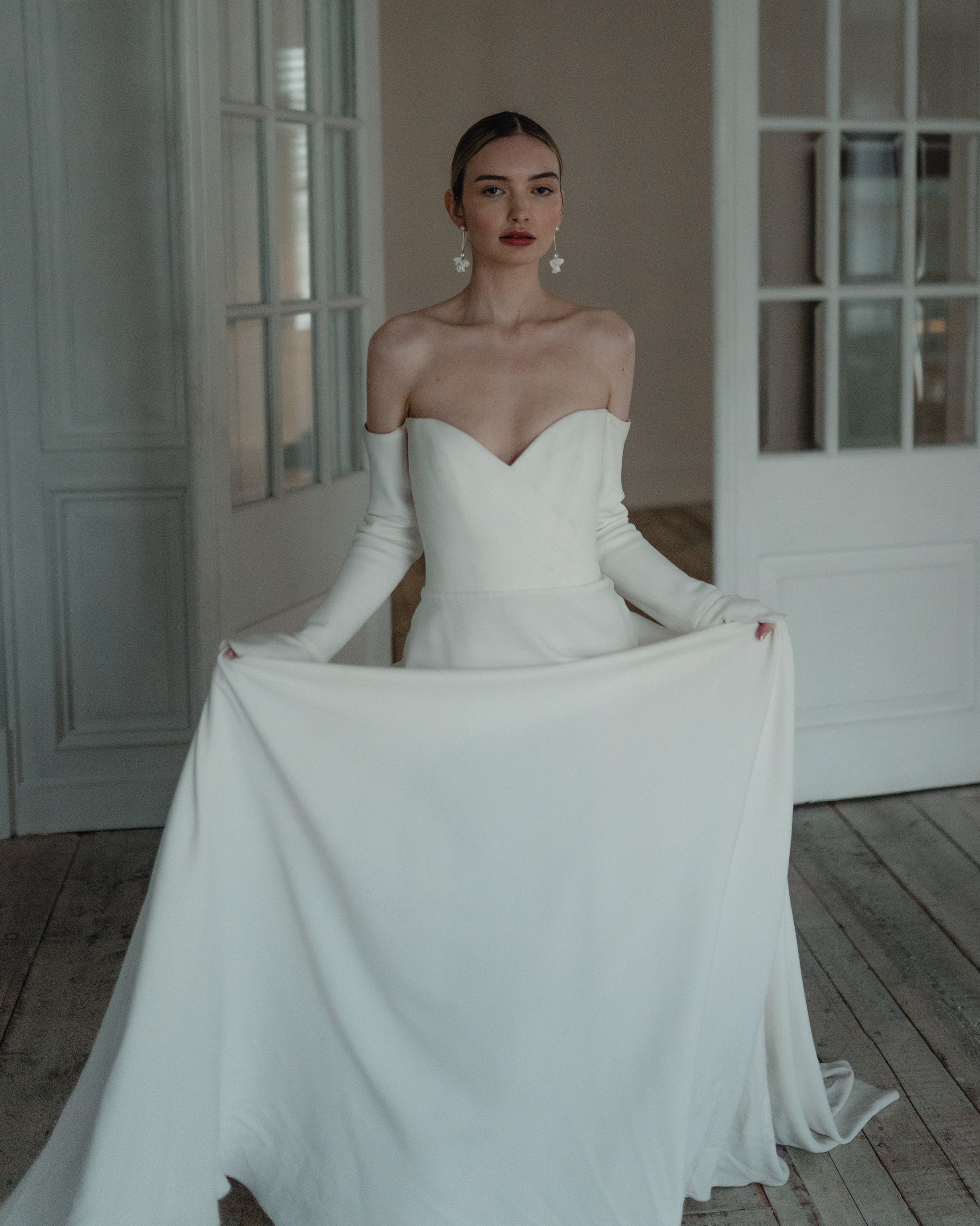 Woman in a white strapless gown holding a long train in a softly lit room.