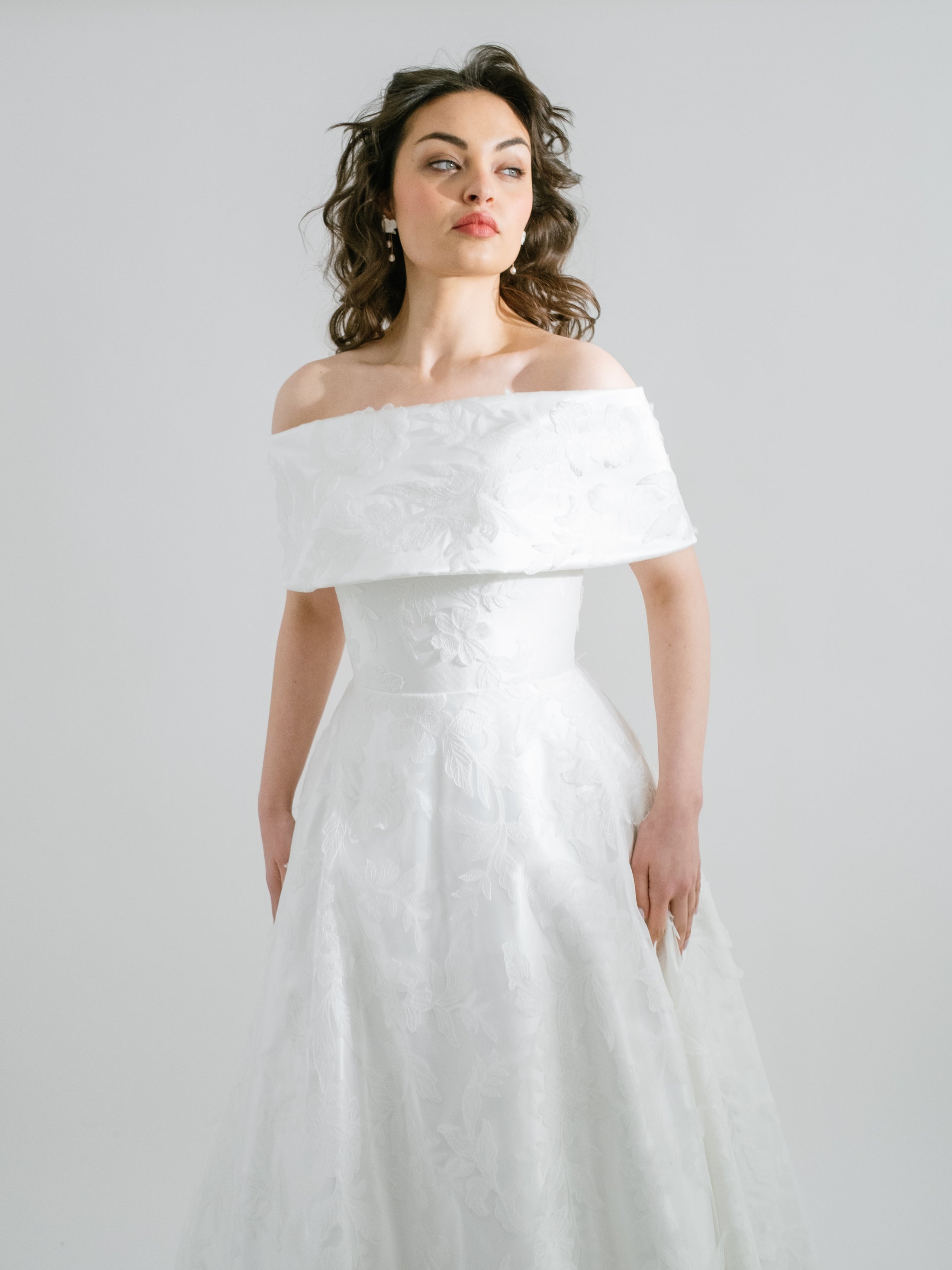 Woman wearing a white off-shoulder wedding dress against a plain background