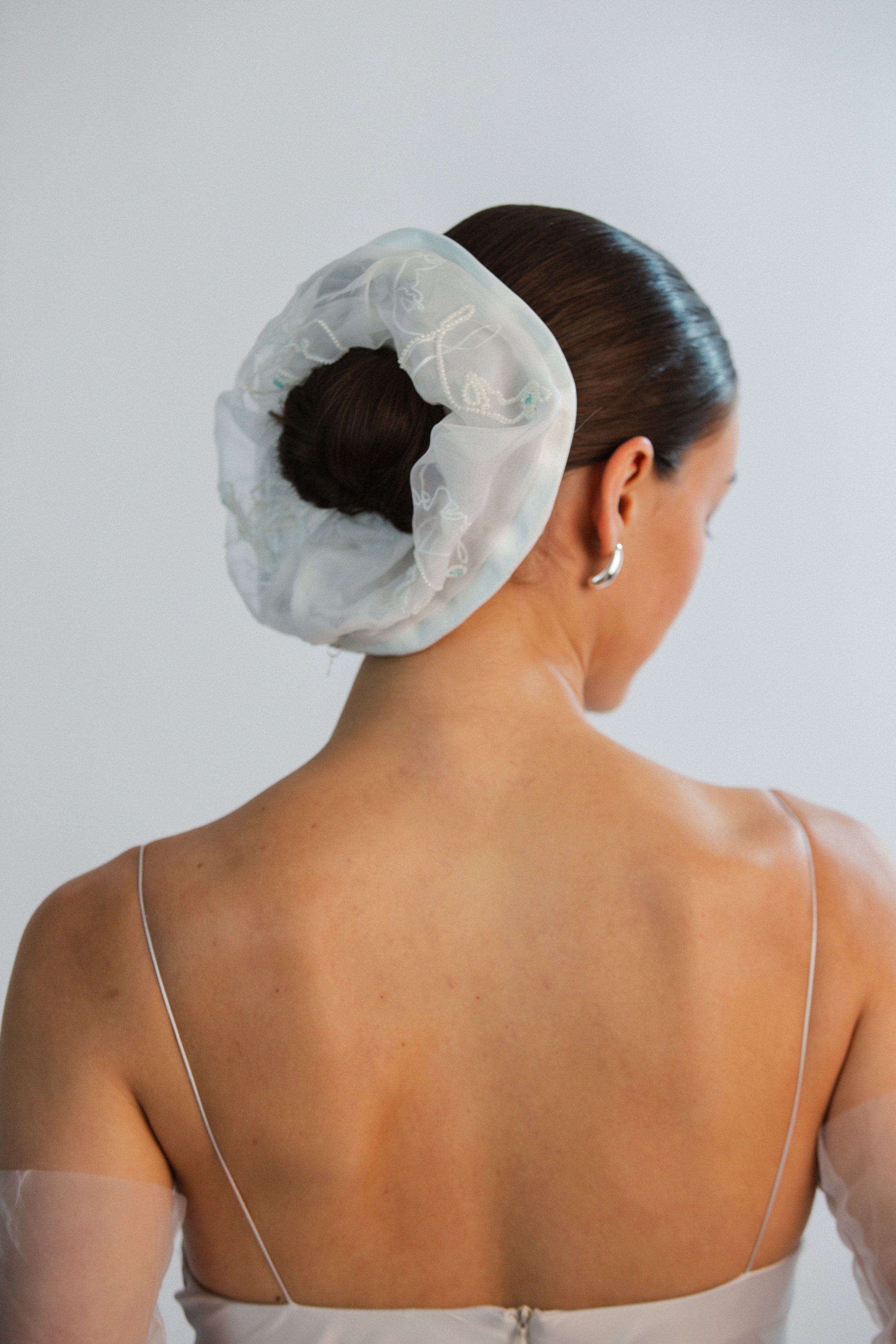 Woman wearing a sheer white bridal headband with a plain background