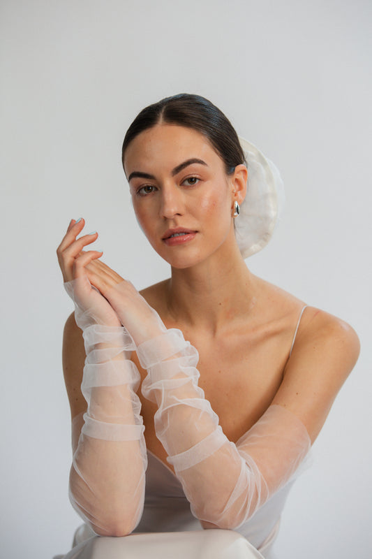Bride wearing sheer white gloves and bridal hair scrunchie against a plain background
