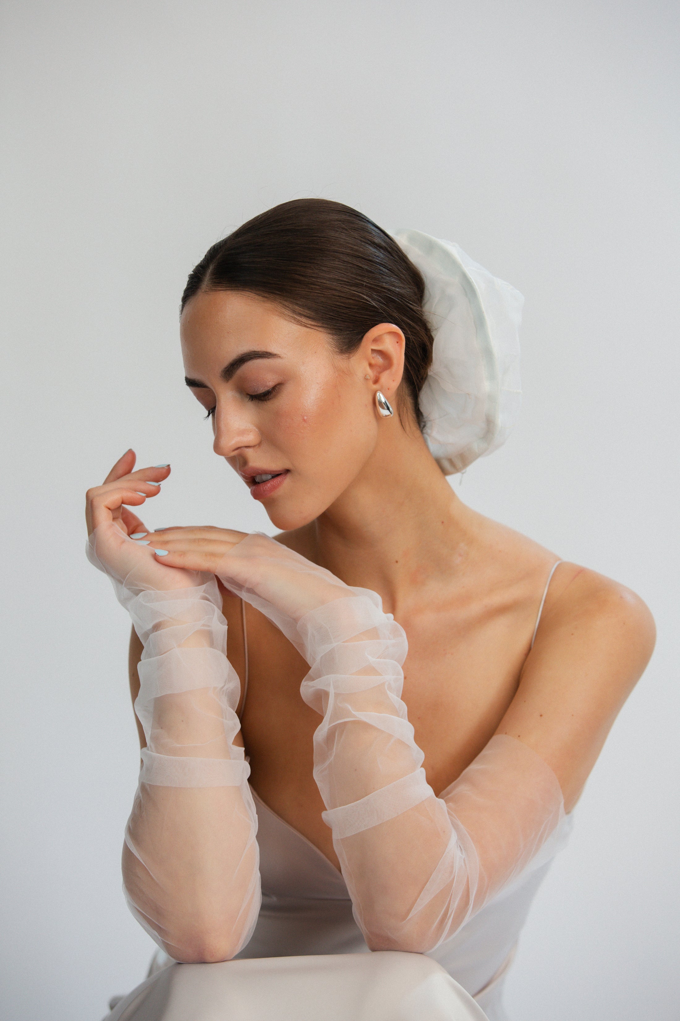 Bride wearing sheer white gloves and bridal hair scrunchie against a plain background