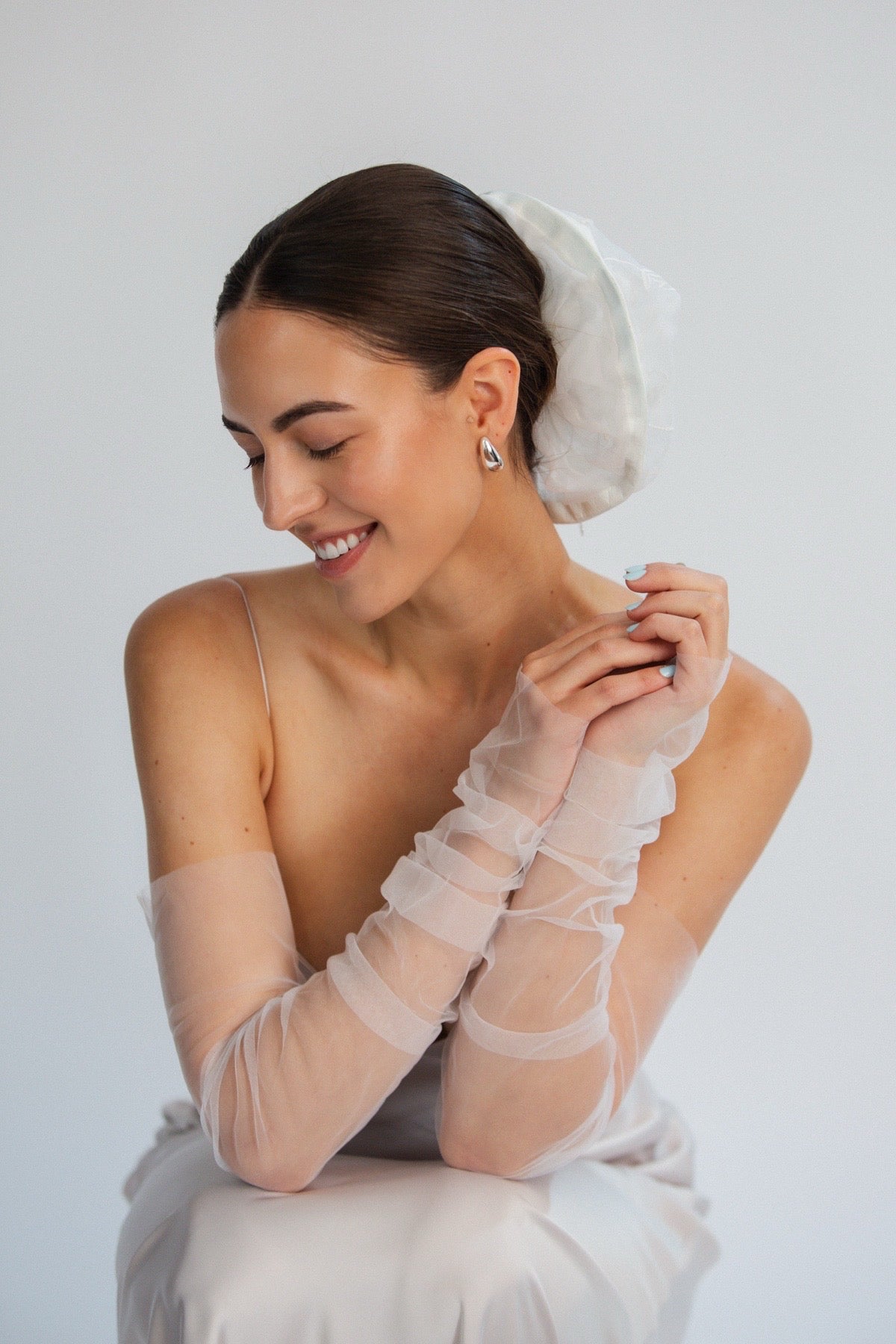 Bride wearing sheer white gloves and bridal hair scrunchie against a plain background