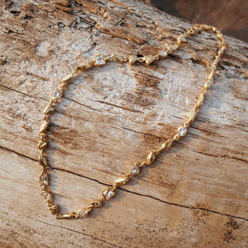 Gold necklace with heart-shaped clasp on a wooden surface