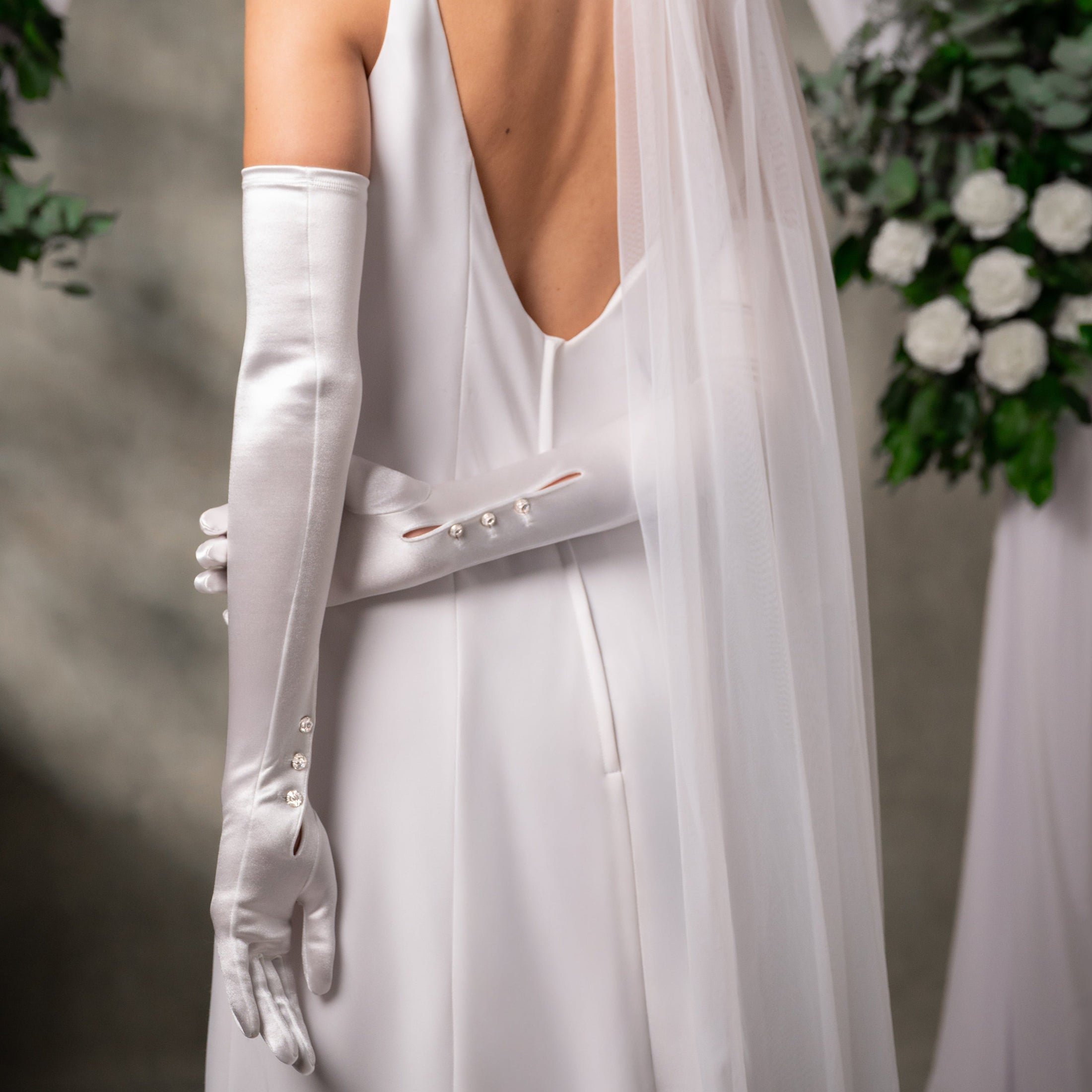 White wedding dress with long gloves and a veil, against a neutral background.