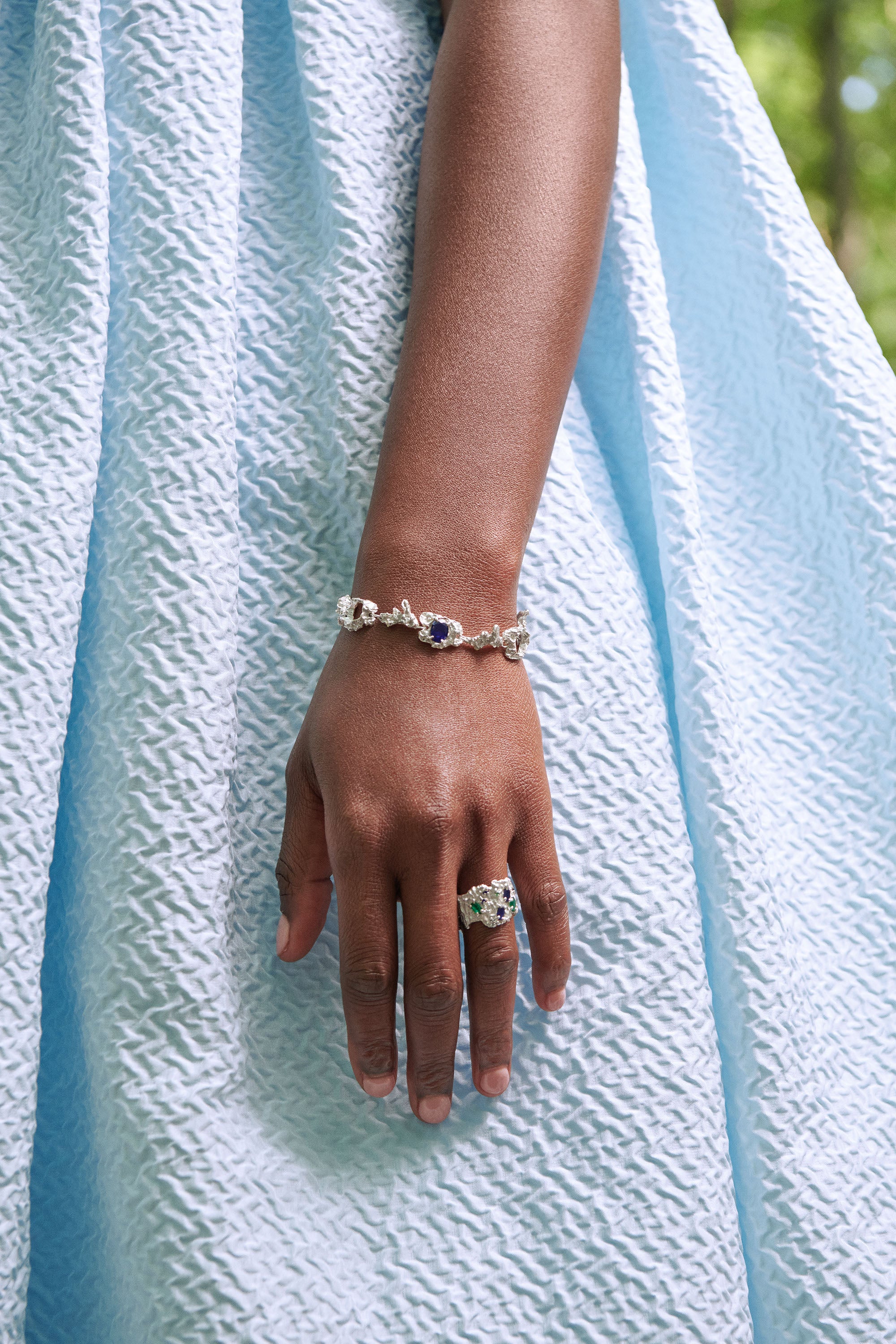 Hand wearing a bracelet and ring on a light blue fabric background