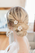 Load image into Gallery viewer, Blonde hair styled in an updo with floral hairpins, blurred indoor background
