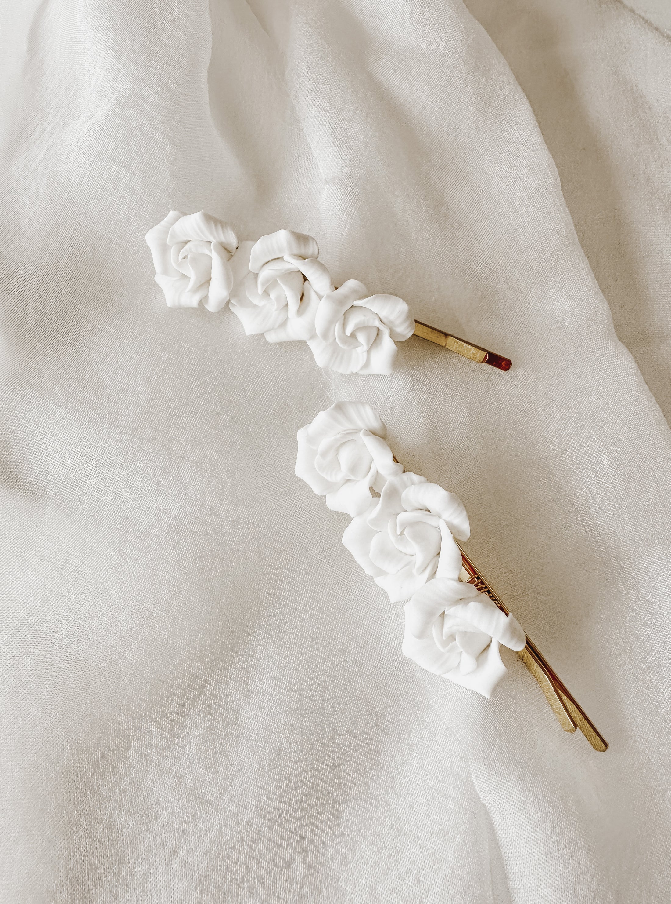Two white floral hairpins on a white fabric background
