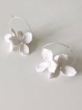 Load image into Gallery viewer, Pair of white floral hoop earrings on a light gray background
