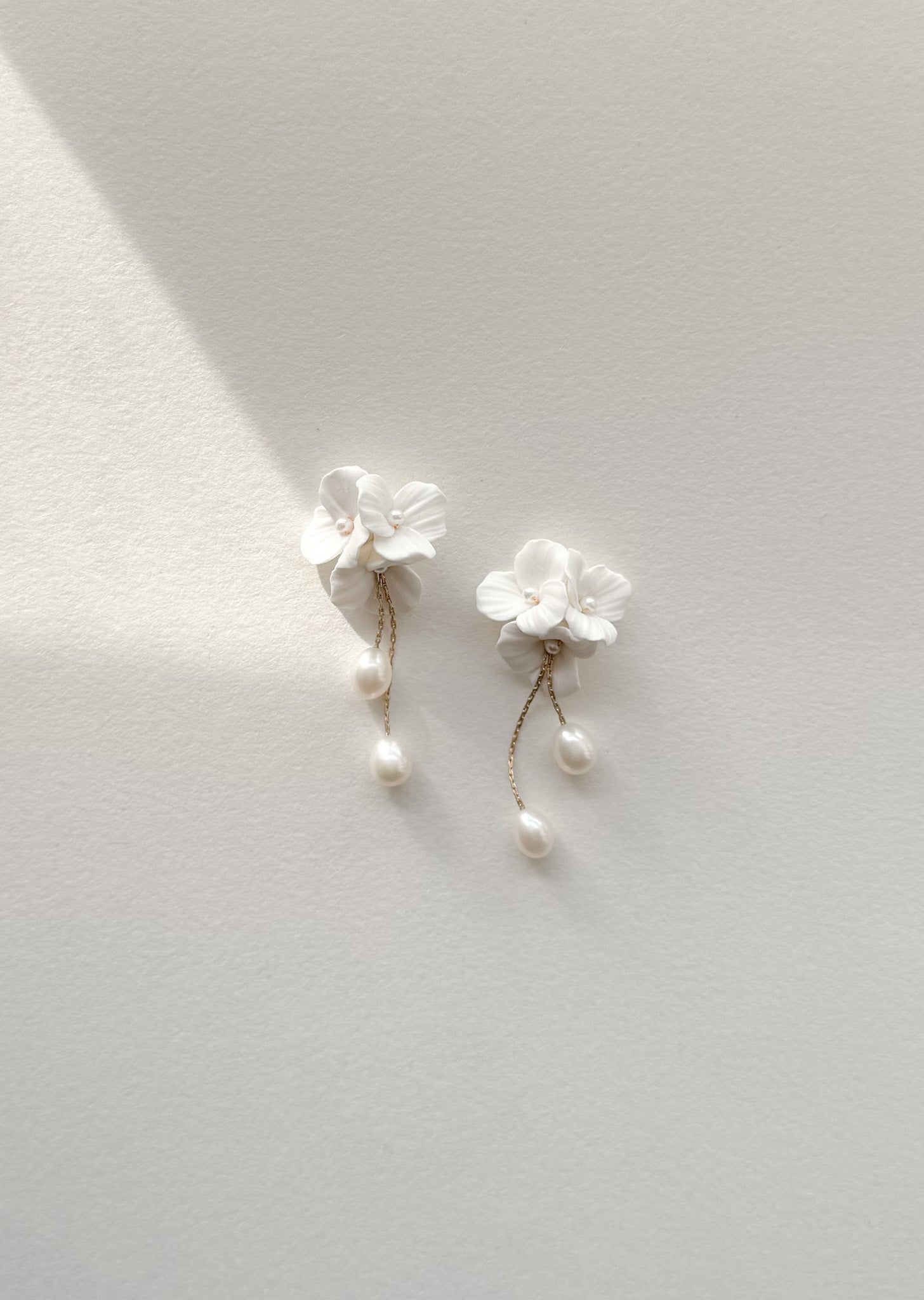 White floral earrings with pearl details on a light gray background