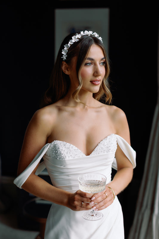 Woman in a white wedding dress holding a glass of champagne, wearing a floral headband.