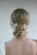 Load image into Gallery viewer, Blonde hair styled in an updo with floral accessories on a plain background
