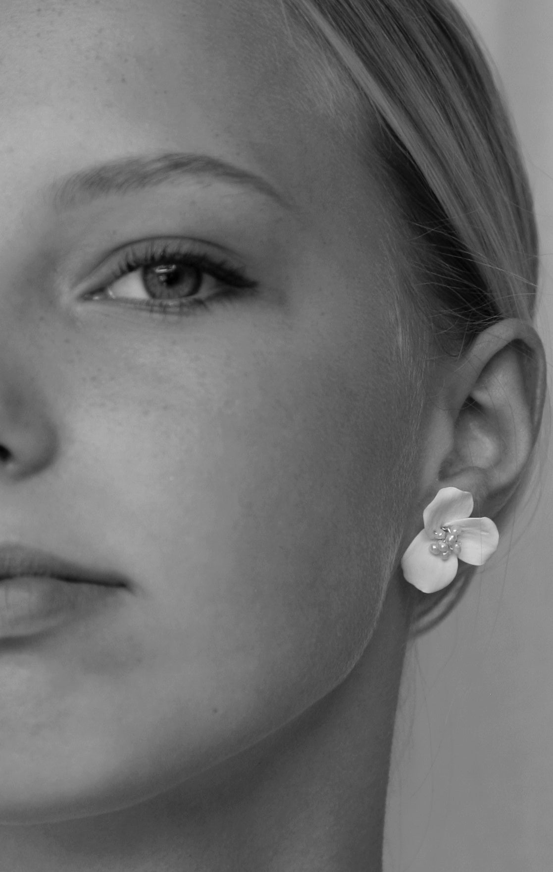 Close-up of a woman wearing a floral earring with a clear gemstone.