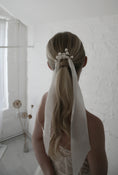 Load image into Gallery viewer, Person with a styled ponytail with a white ribbon in a minimalistic room.
