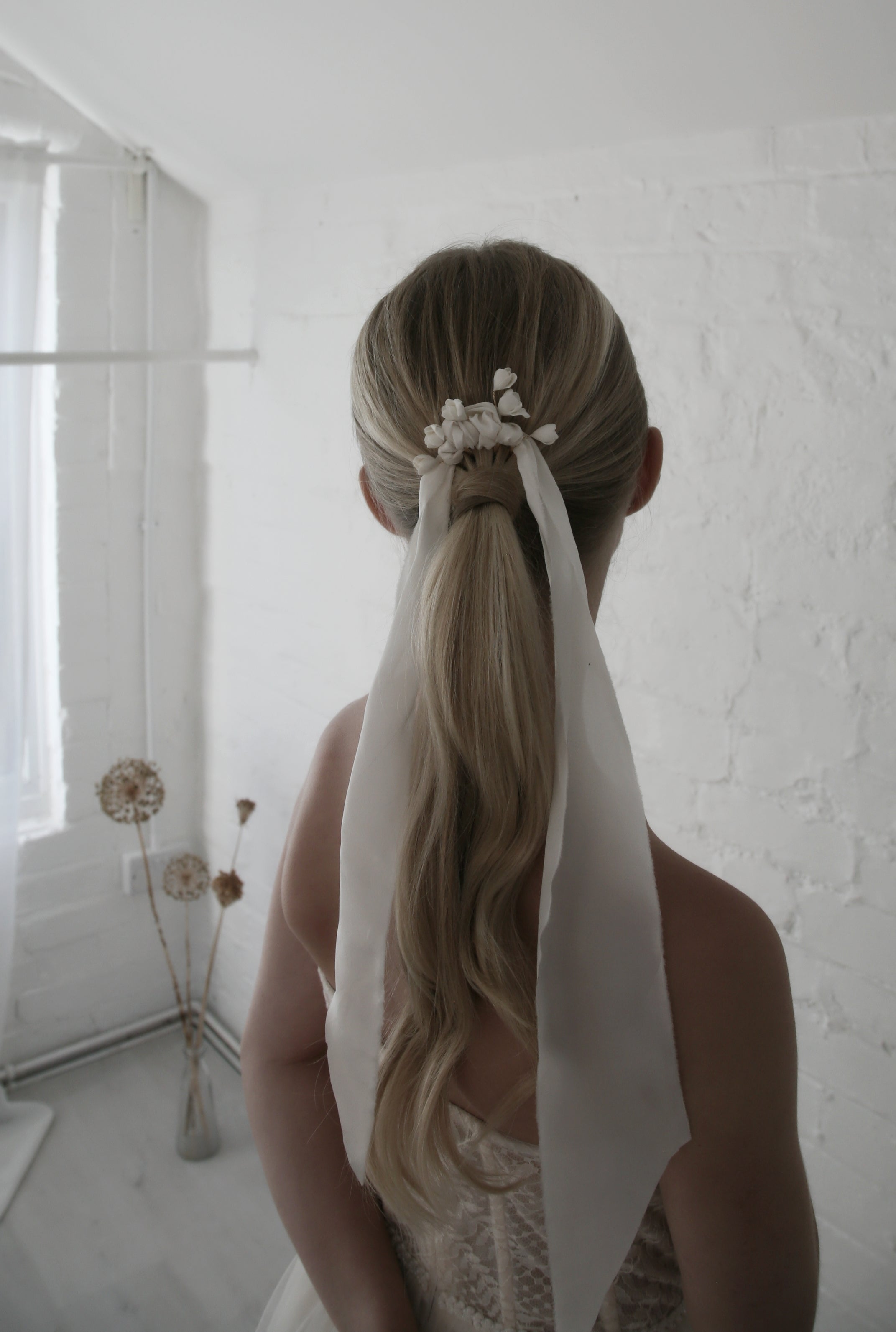 Person with a styled ponytail with a white ribbon in a minimalistic room.