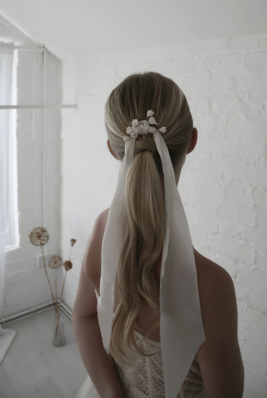 Person with a styled ponytail with a white ribbon in a minimalistic room.
