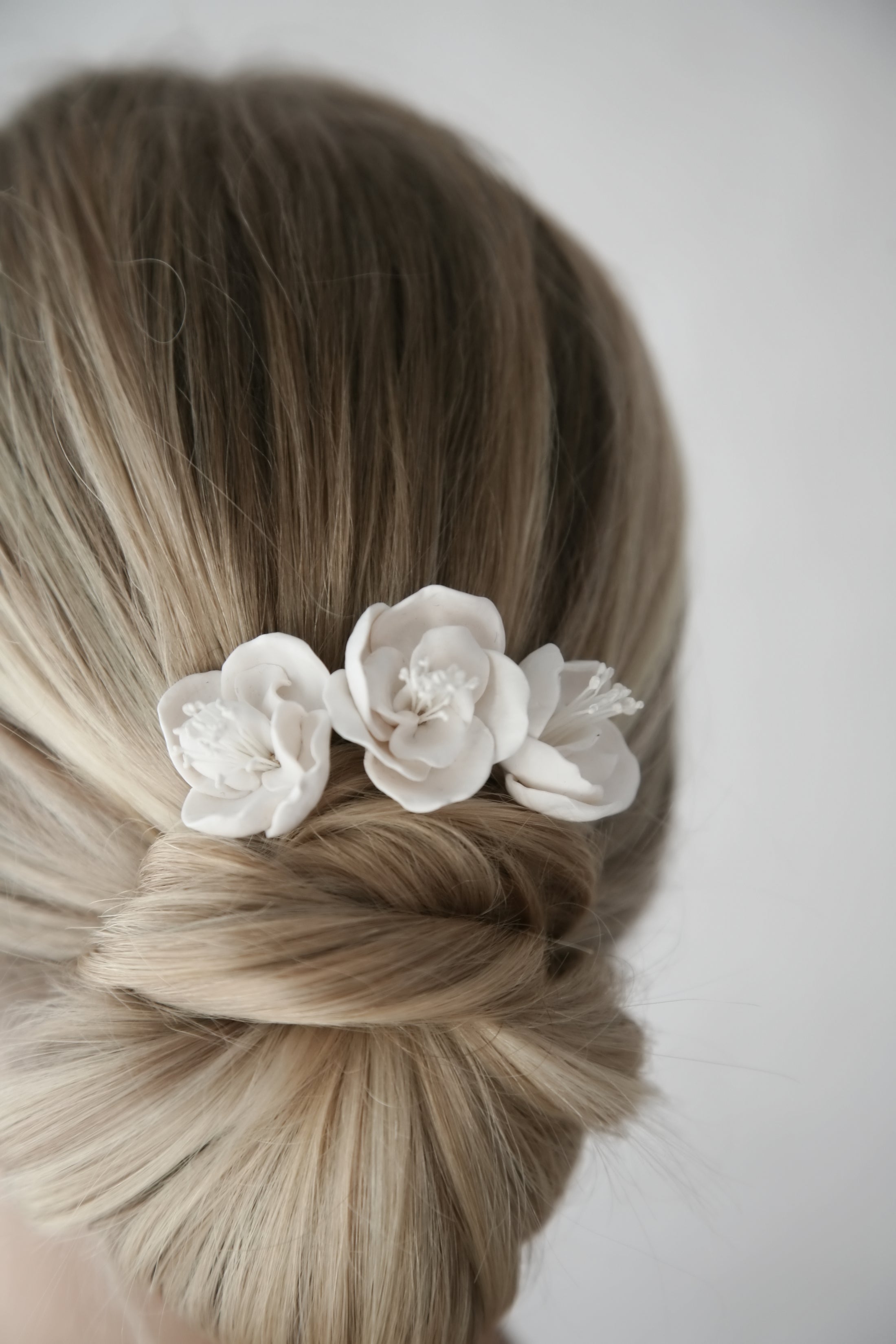 Blonde hair styled in an updo with white floral hair accessory on a plain background