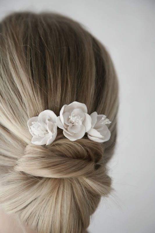 Blonde hair styled in an updo with white floral hair accessory on a plain background