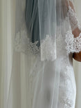Load image into Gallery viewer, close uo of white wedding dress with a long lace veil in front of a white curtain.
