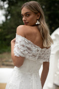 Load image into Gallery viewer, Woman wearing a white lace off-shoulder dress with a blurred natural background
