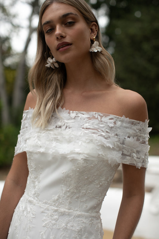 Woman wearing an off-shoulder white dress with floral details outdoors.