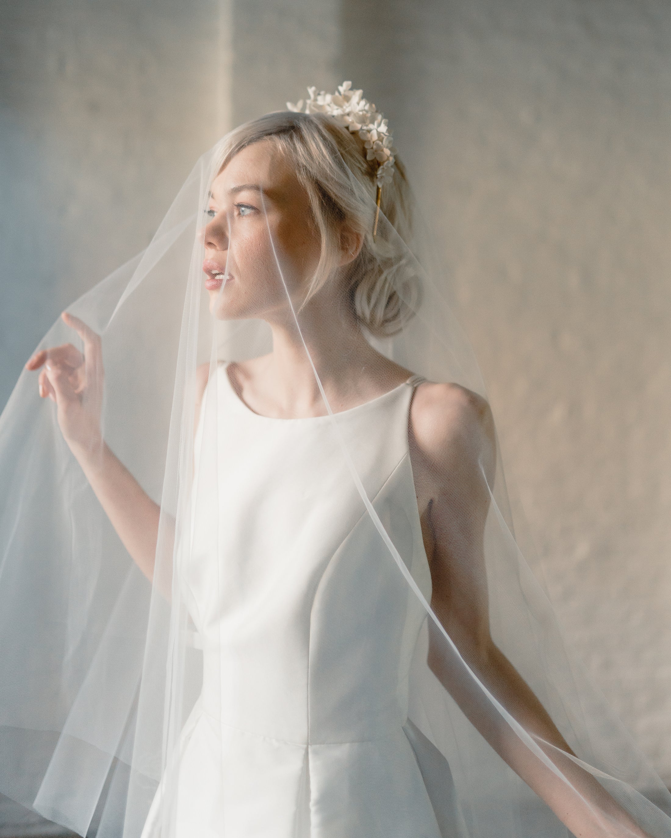 Woman in a white wedding dress with a veil against a neutral background