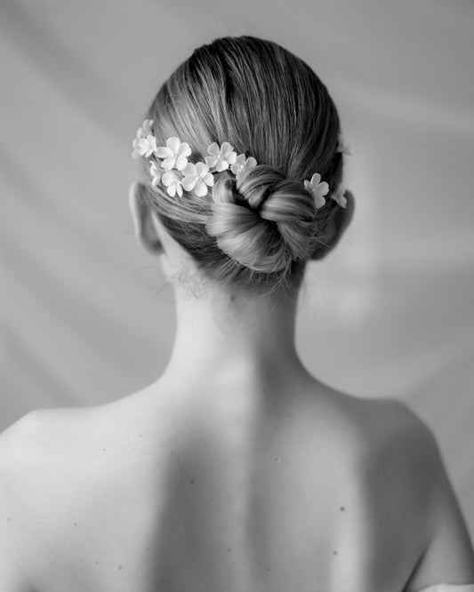 Black and white photo of a woman's head with a braided hairstyle and floral hair accessory.