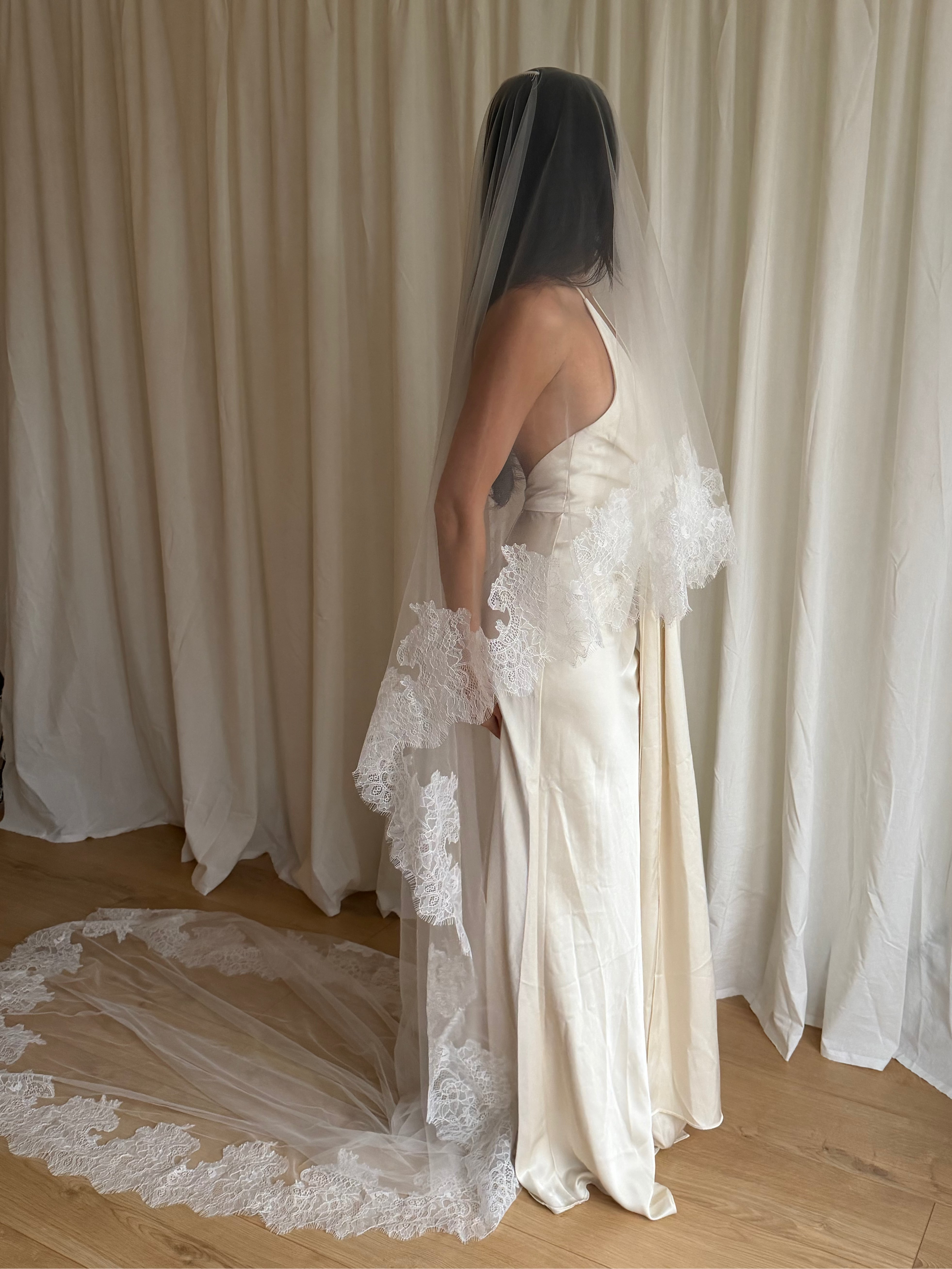 Bride wearing a white wedding dress with a lace veil against a white curtain background.