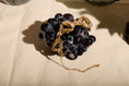 Load image into Gallery viewer, Gold bracelet on a cluster of dark grapes on a beige fabric background

