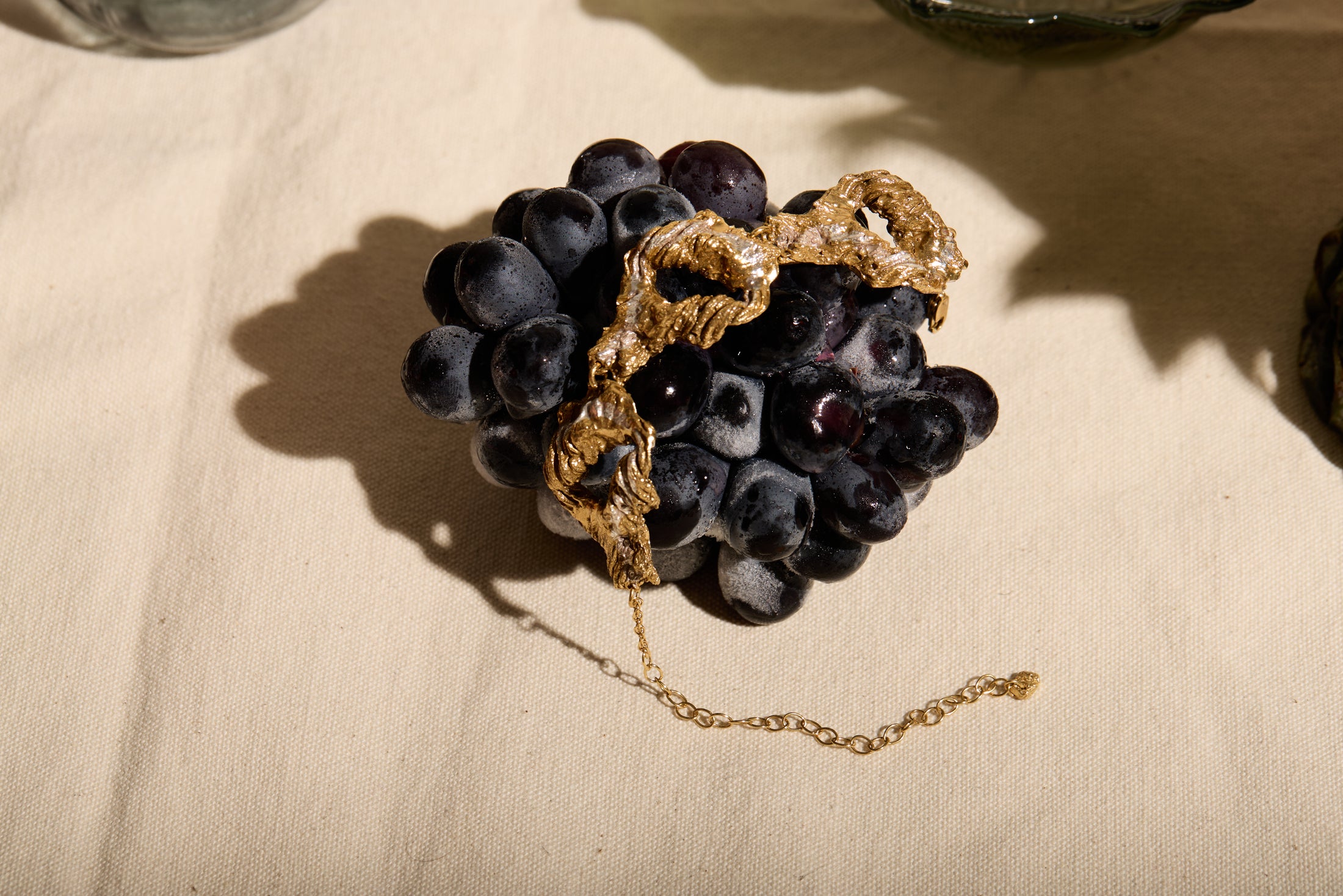 Gold bracelet on a cluster of dark grapes on a beige fabric background