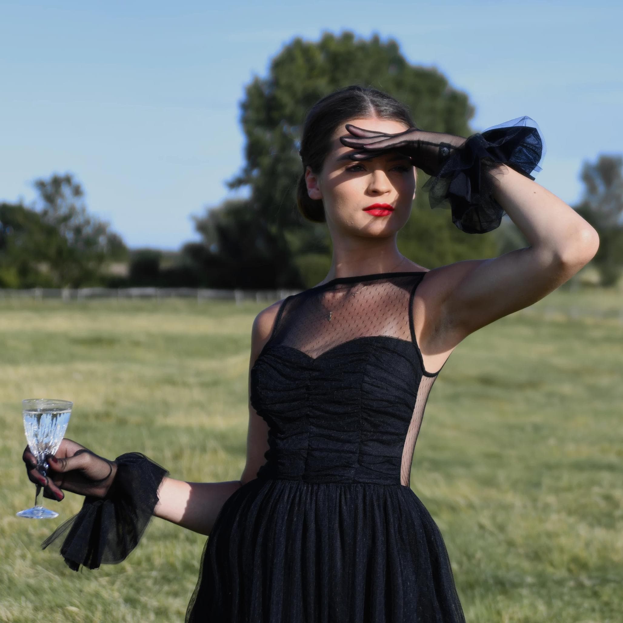 woman wearing Cornelia James tulle black bridal gloves with harlequin cuff detail.  background is a field. 