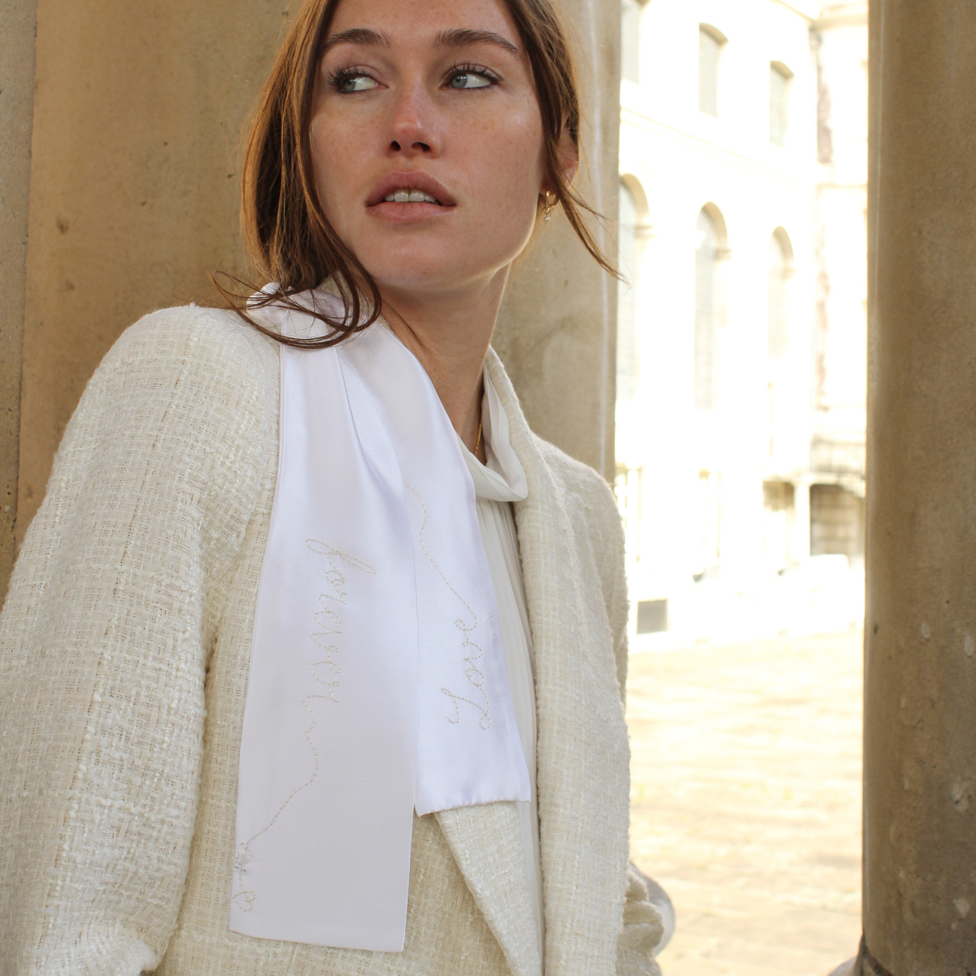 Woman wearing a light-colored blazer with a white hair ribbon against a beige wall.