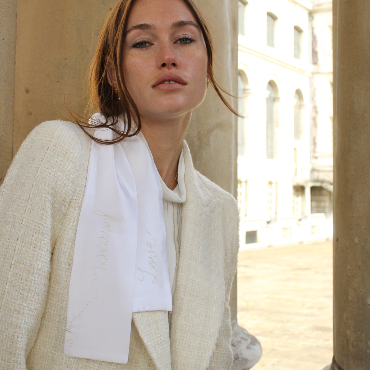 Woman wearing a light-colored blazer with a white hair ribbon against a beige wall.