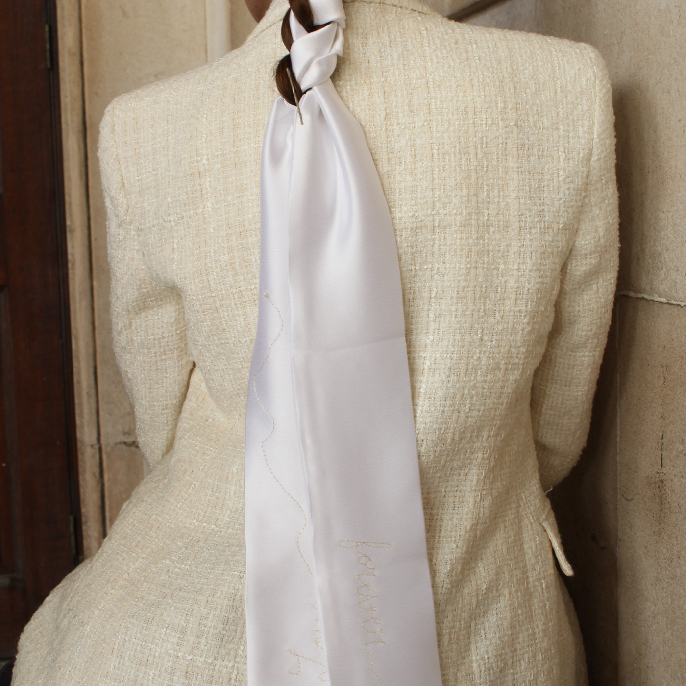 Woman wearing a light-colored blazer with a white hair ribbon against a beige wall.