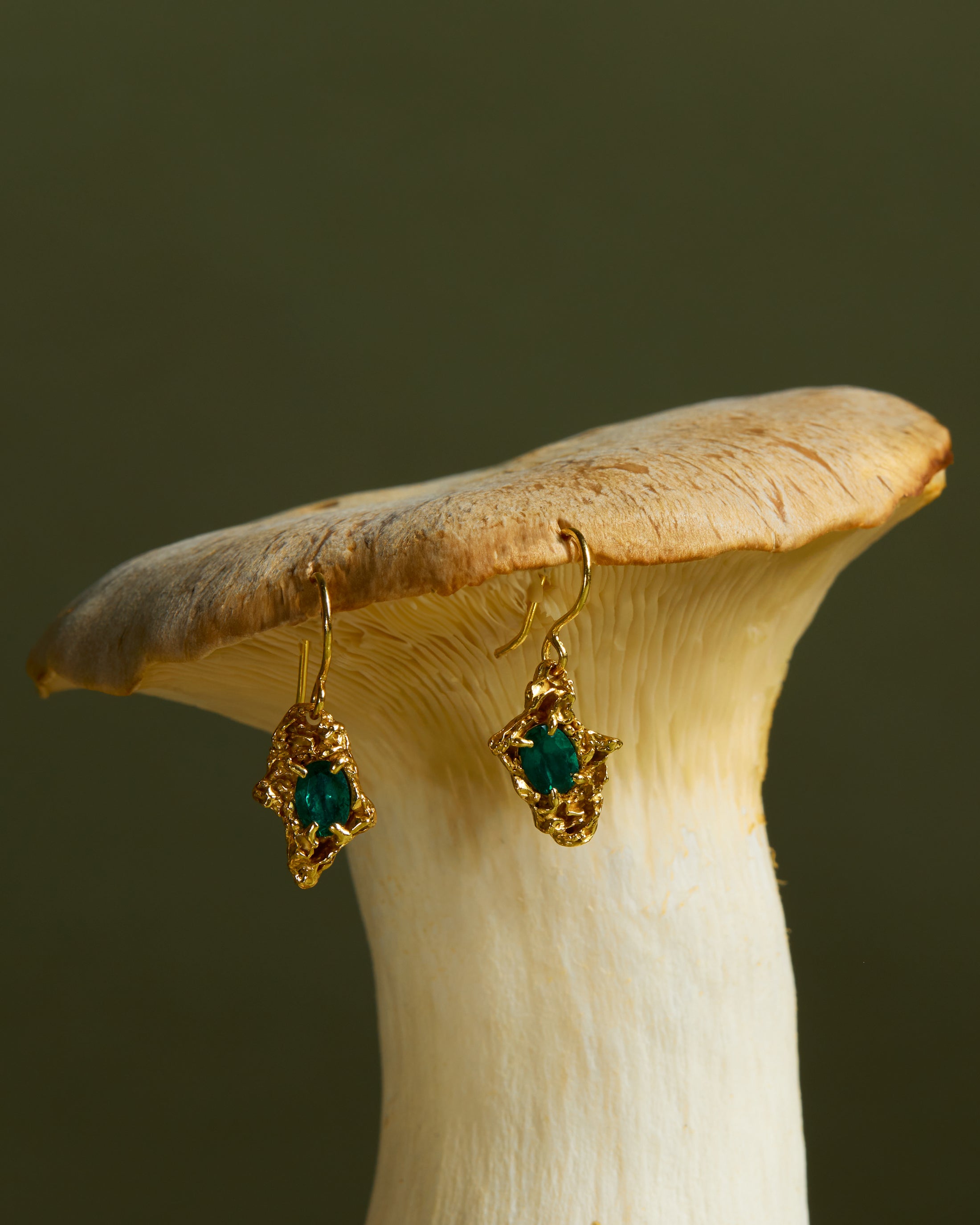 Gold earrings with emeralds on a mushroom