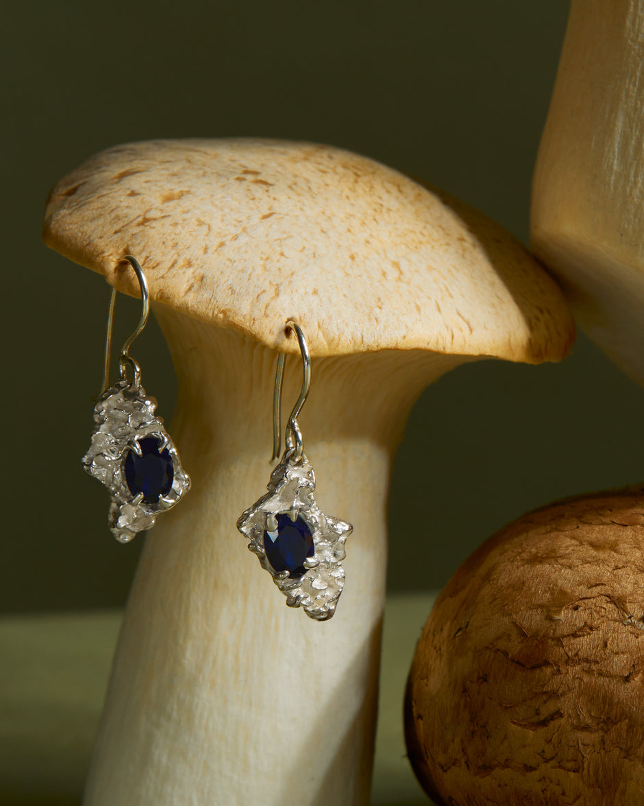 Silver earrings with sapphire on a wooden mushroom