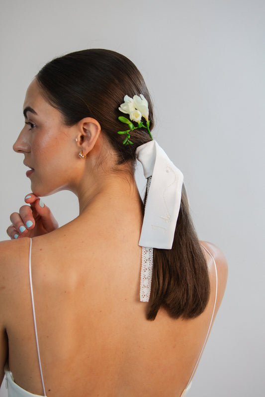Woman with a floral hair accessory and white bridal bow in her hair against a plain background