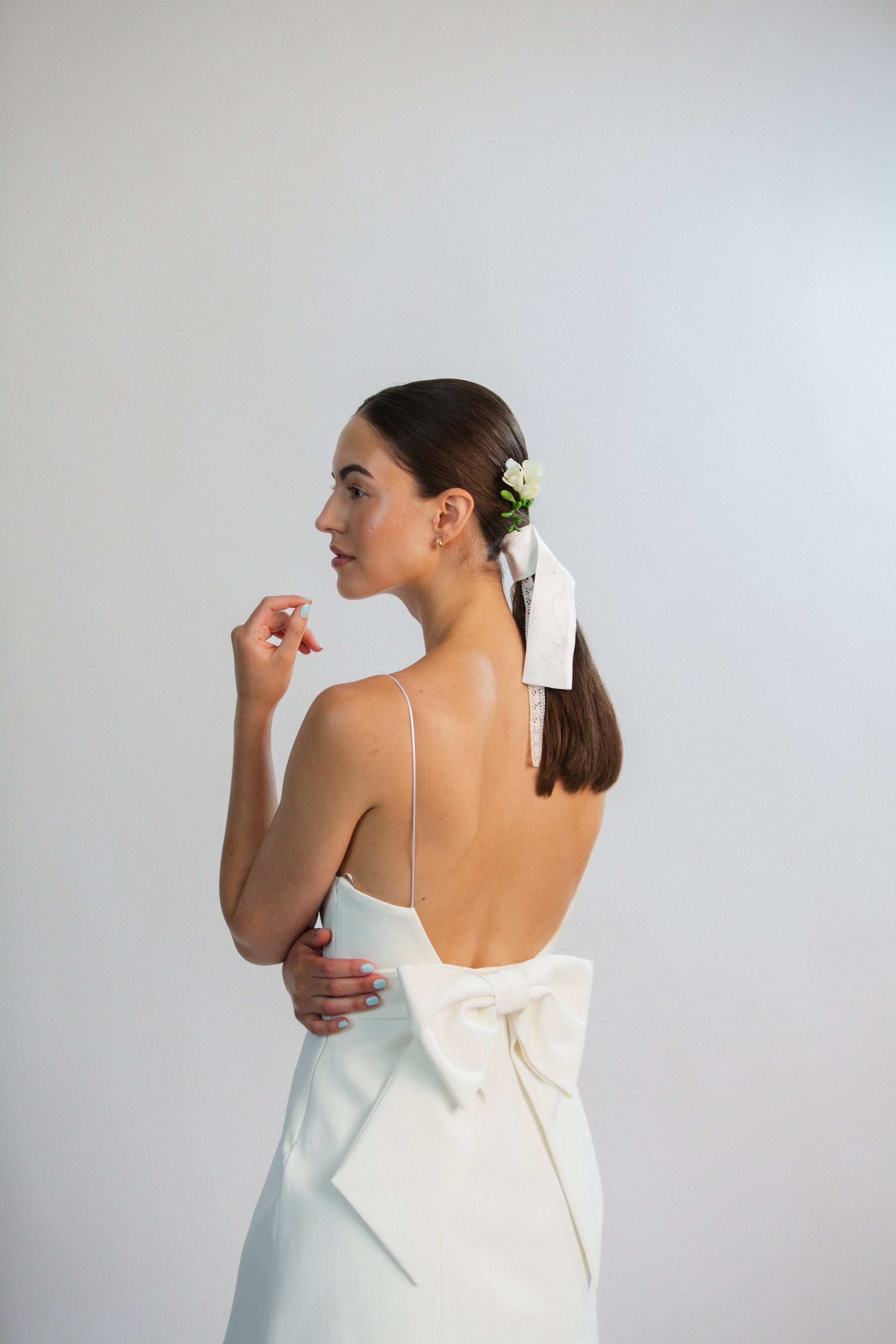 Woman in a white dress with a bow, standing against a plain background