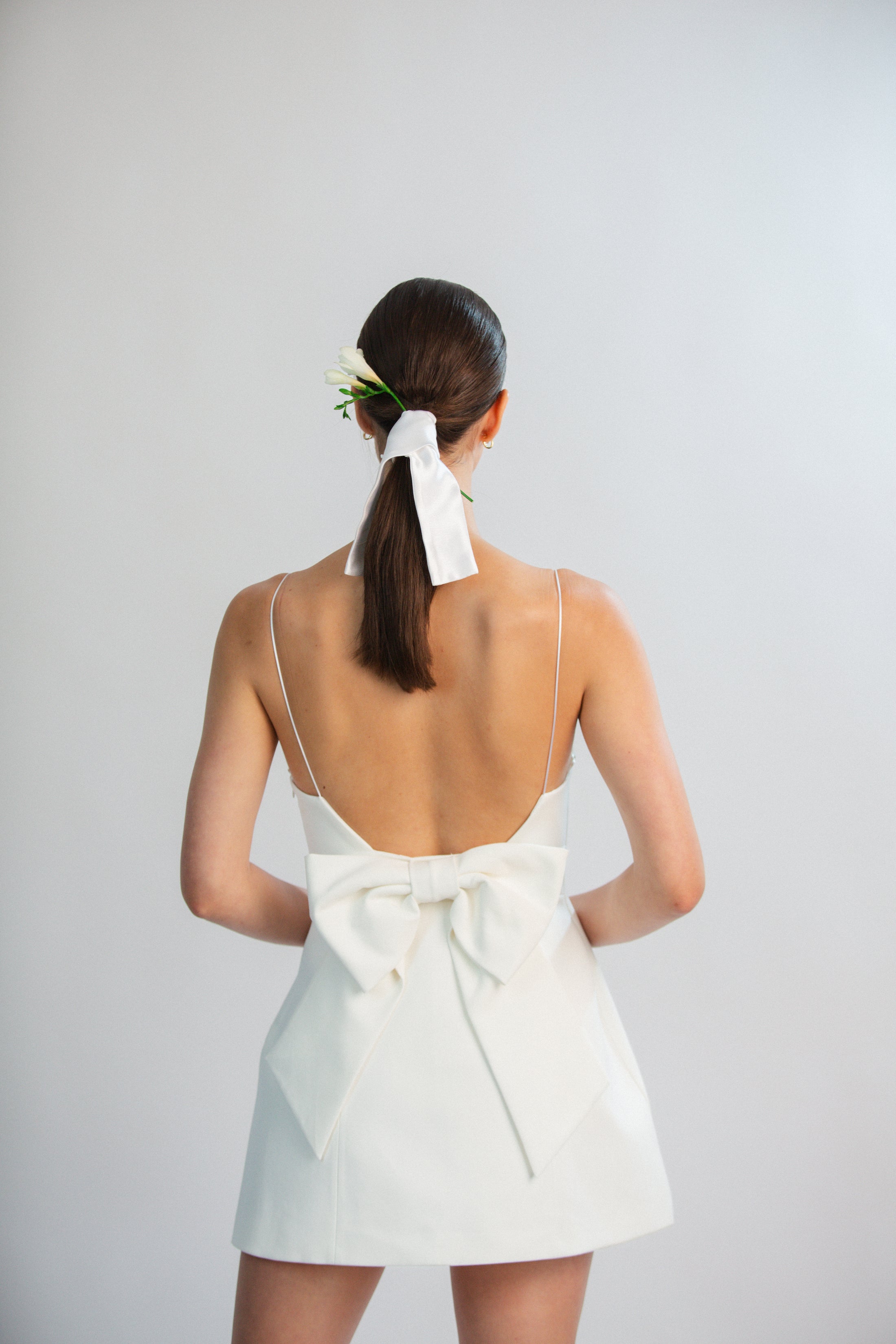 Woman wearing a white dress with a bow at the back on a plain background
