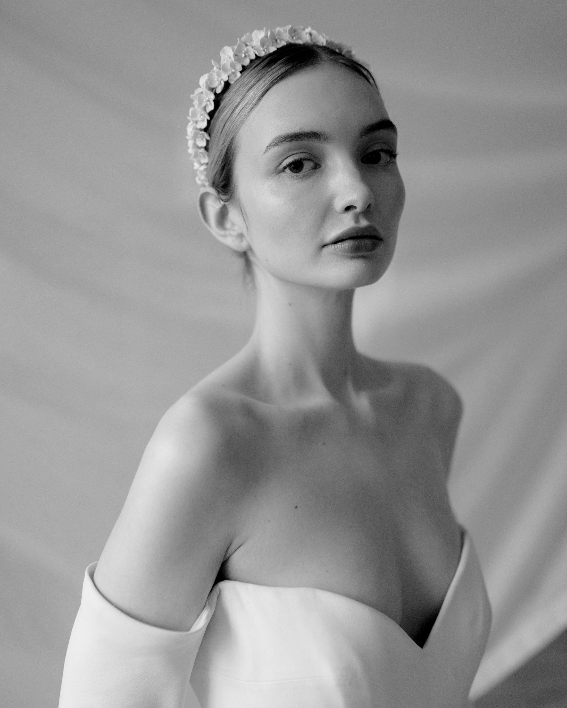 Black and white portrait of a woman wearing a floral headband against a plain background
