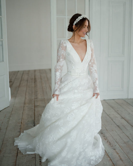Woman in a white wedding dress standing in a room with wooden flooring.