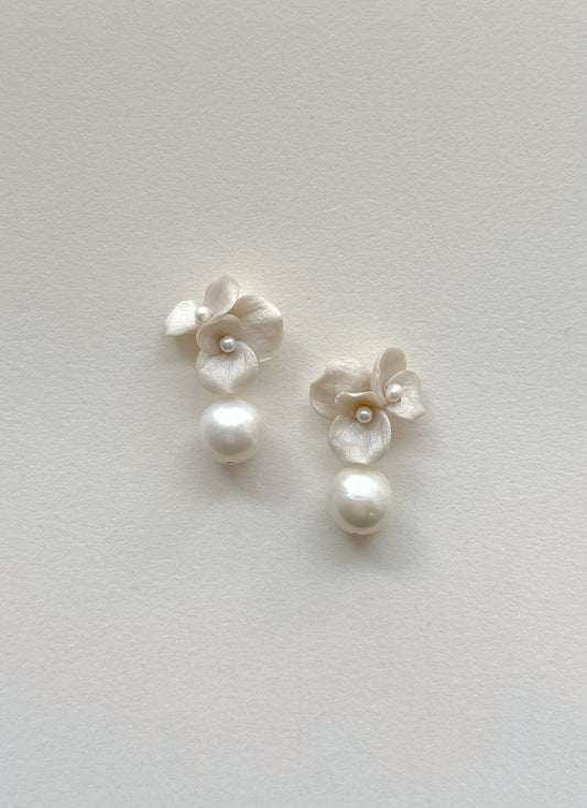 Pair of white floral earrings with pearls on a light gray background