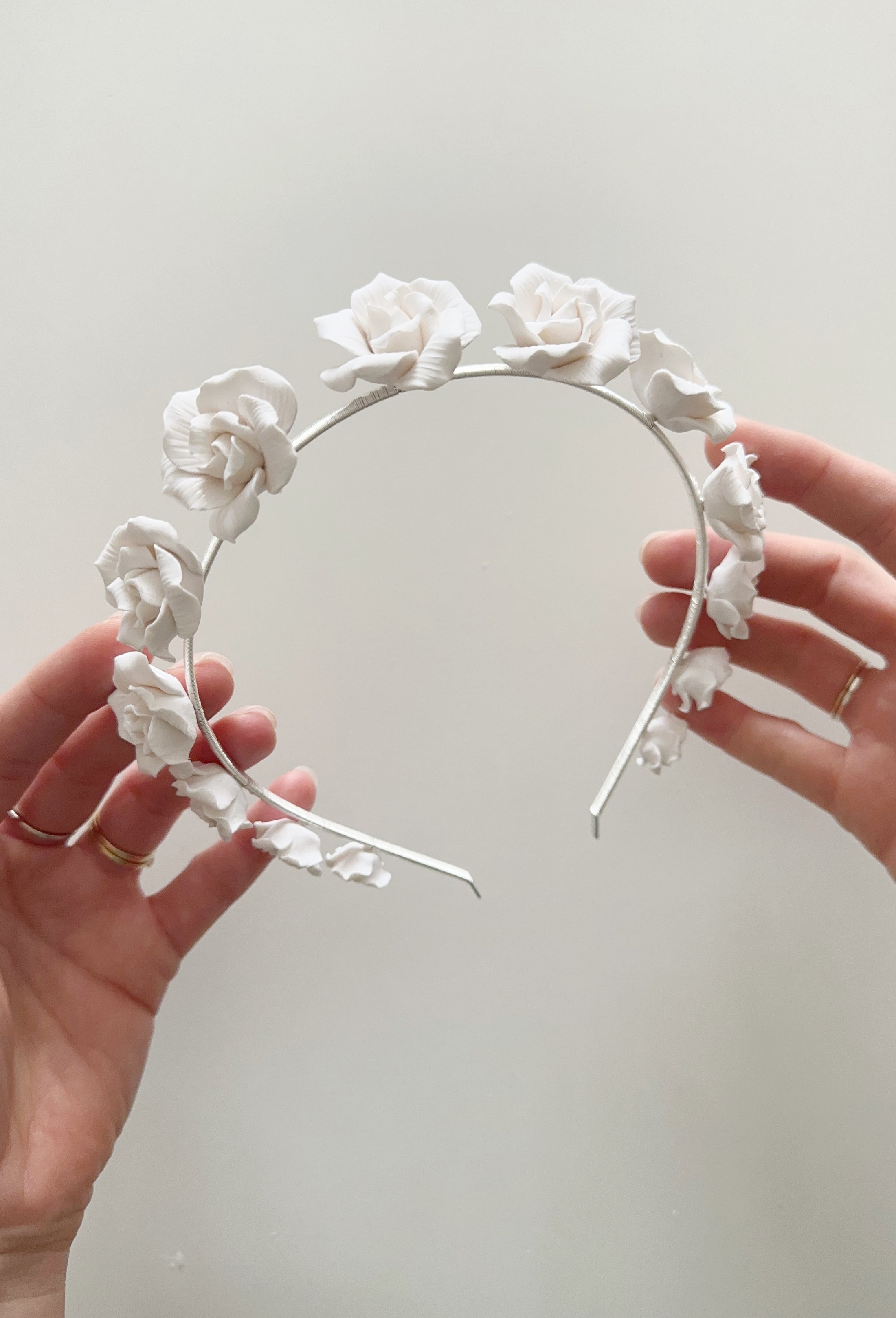 White floral headband held by hands against a light gray background