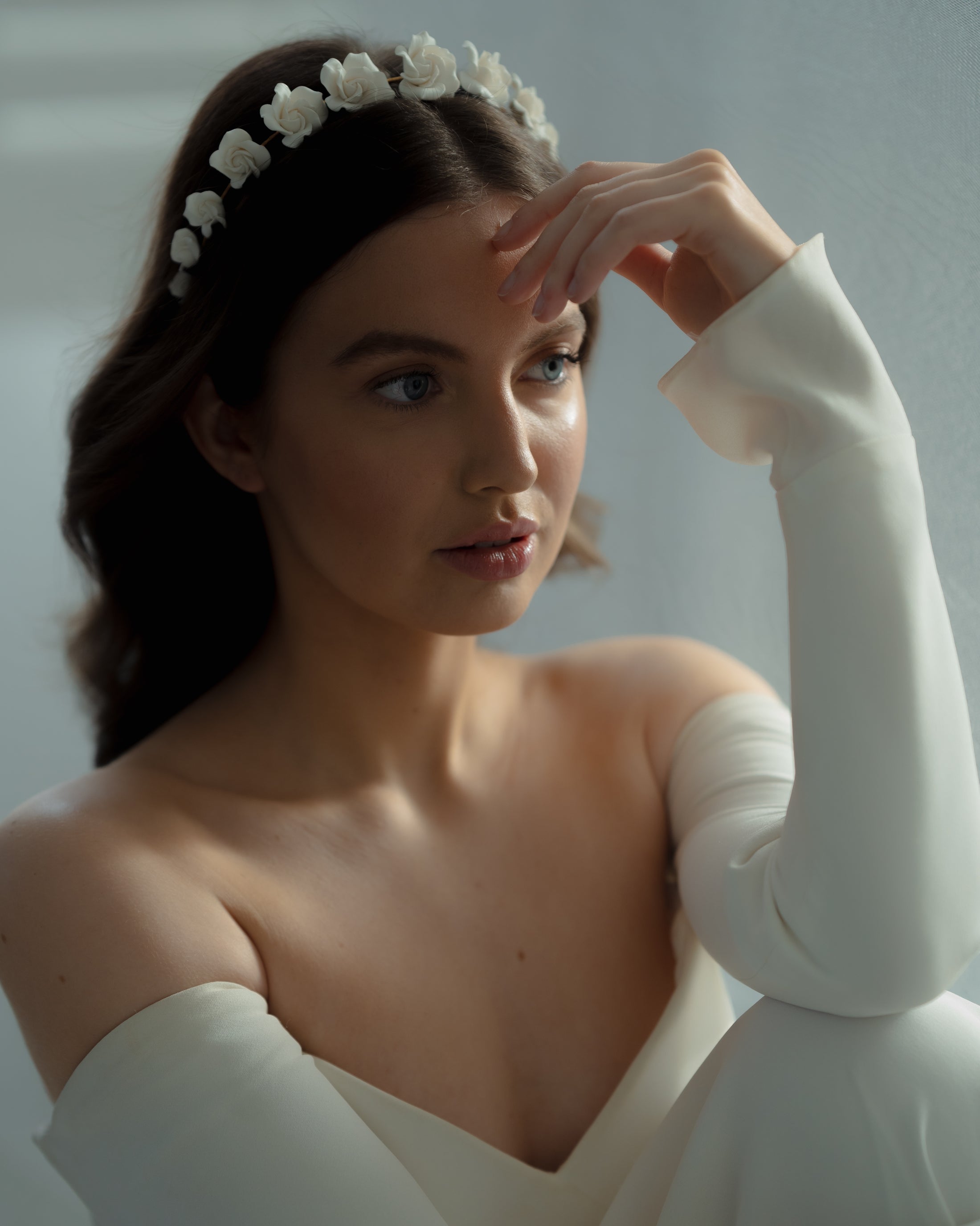 Woman in a white dress with a floral headband against a neutral background